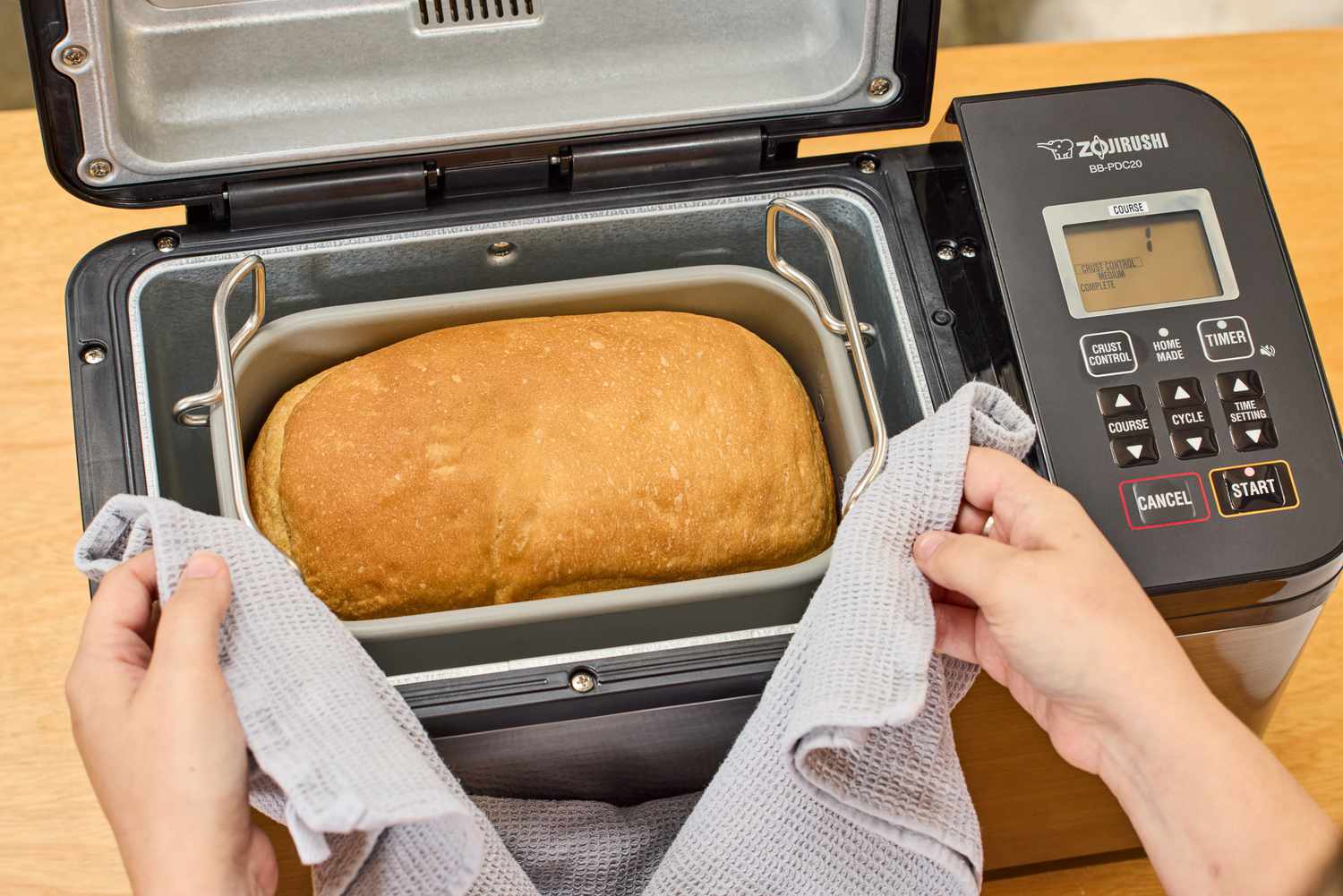 A person using a towel to remove a filled basket from the Zojirushi Home Bakery Virtuoso Plus Bread Maker