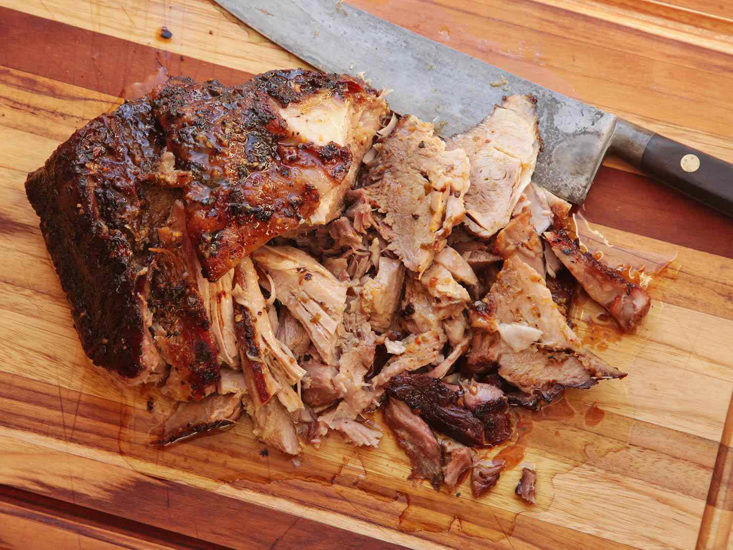 Cuban-Style Roast Pork Shoulder With Mojo Recipe on a cutting board, being shredded with a knife. 