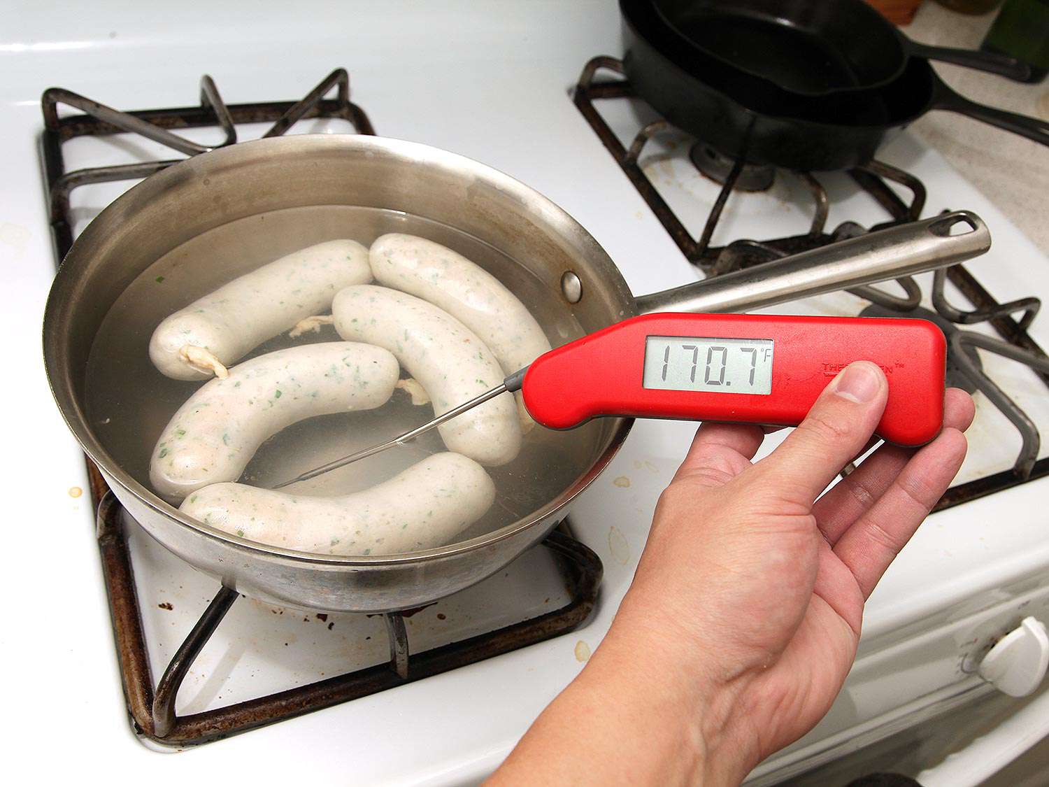 Sausage links are poached in a saucepan full of water. A thermometer reads the water at 170F.