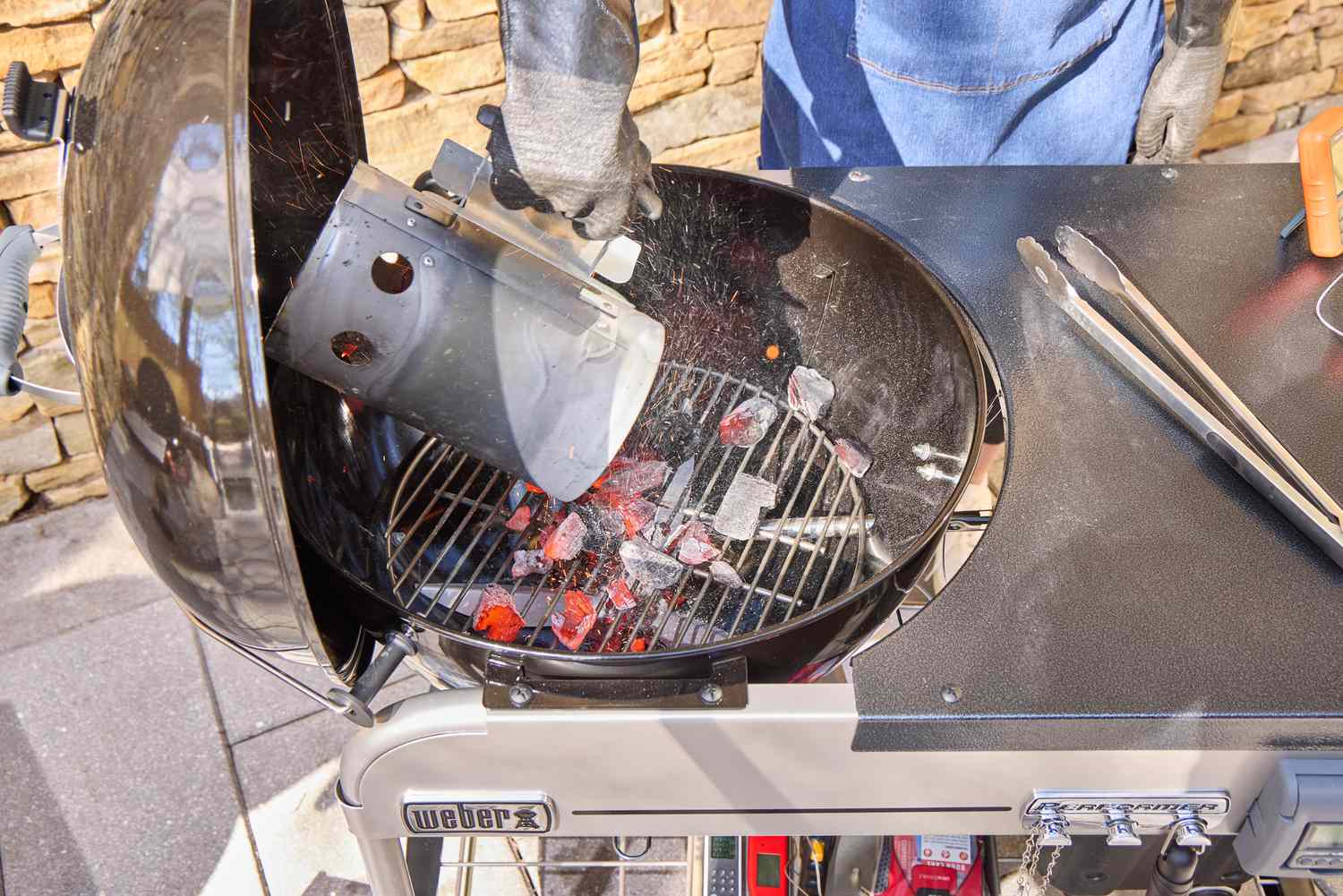 A person adding hot coals onto the Weber Performer Deluxe Charcoal Grill 22
