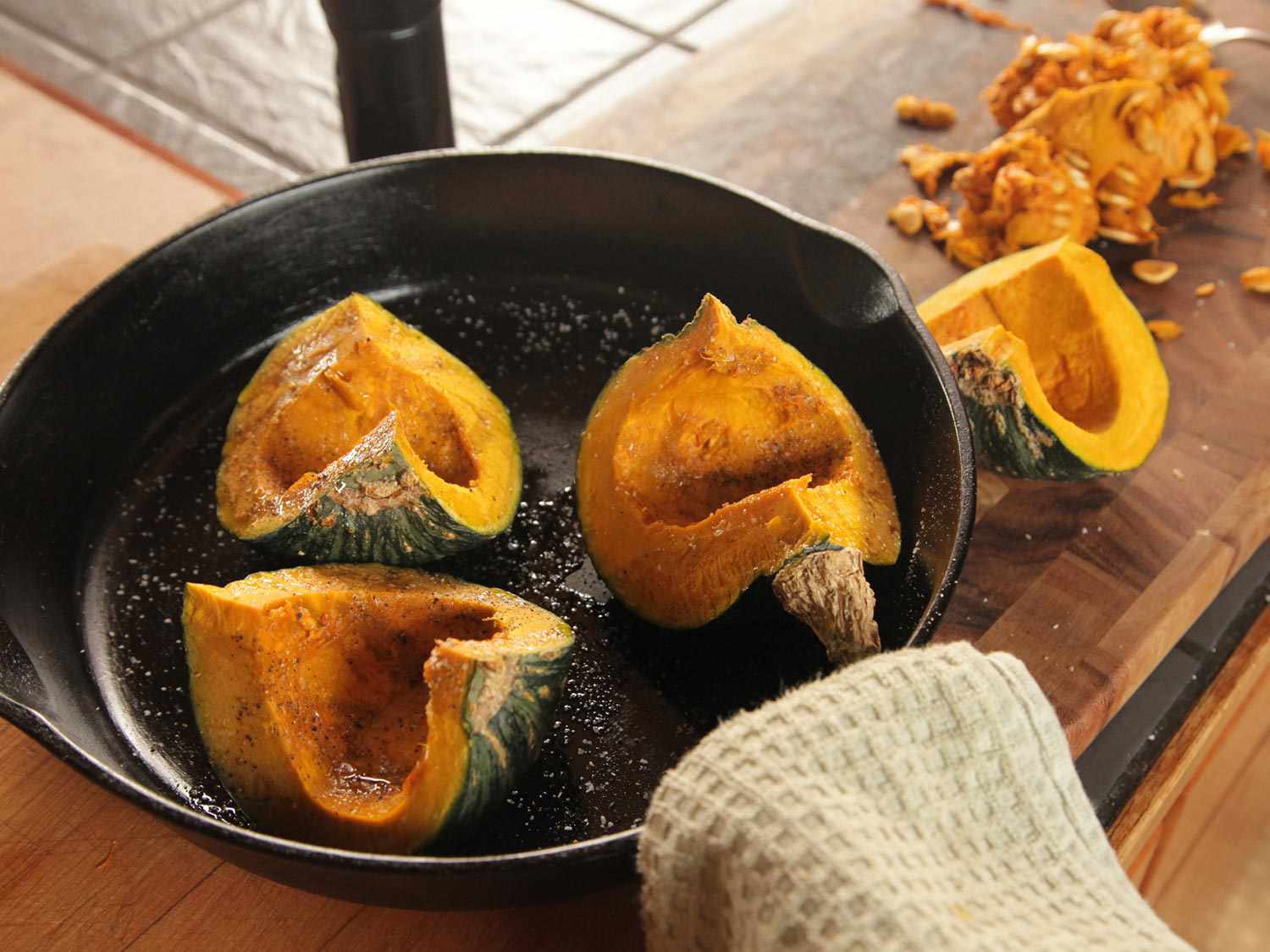 Three seasoned, seeded, and quartered pieces of kabocha squash in a cast iron skillet, ready to roast. (The fourth seeded quarter is set aside.)