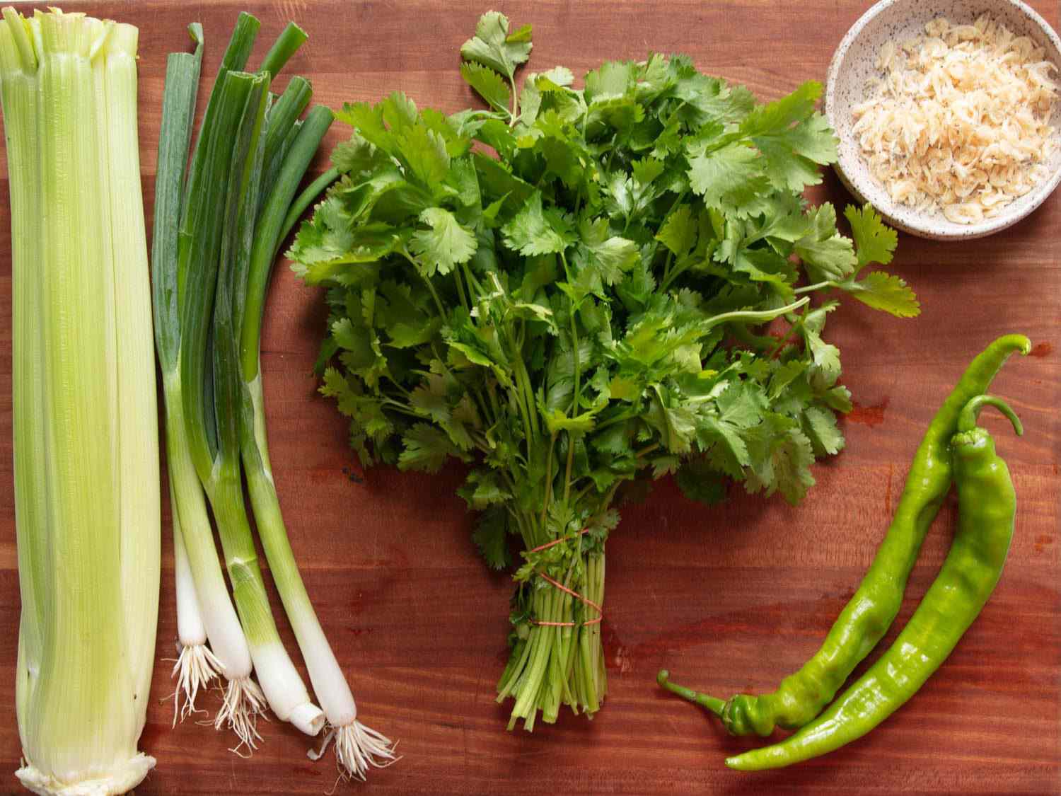 Overhead view of ingredients for tiger salad. From left to right: Celery, scallions, cilantro, long hot pepper, dried shrimp.