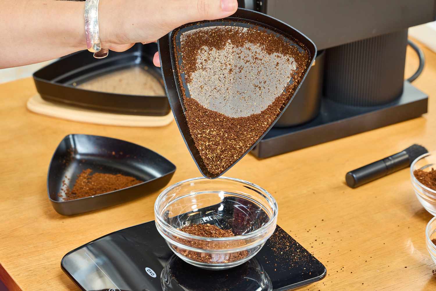 A person weighs coffee grounds from the Fellow Ode Gen 2 Coffee Grinder on a food scale