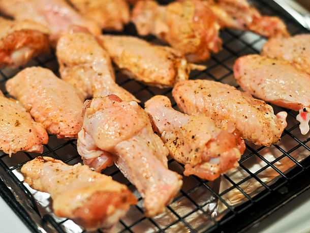 Seasoned, uncooked chicken wings on a black wire rack set over a sheet of aluminum foil.