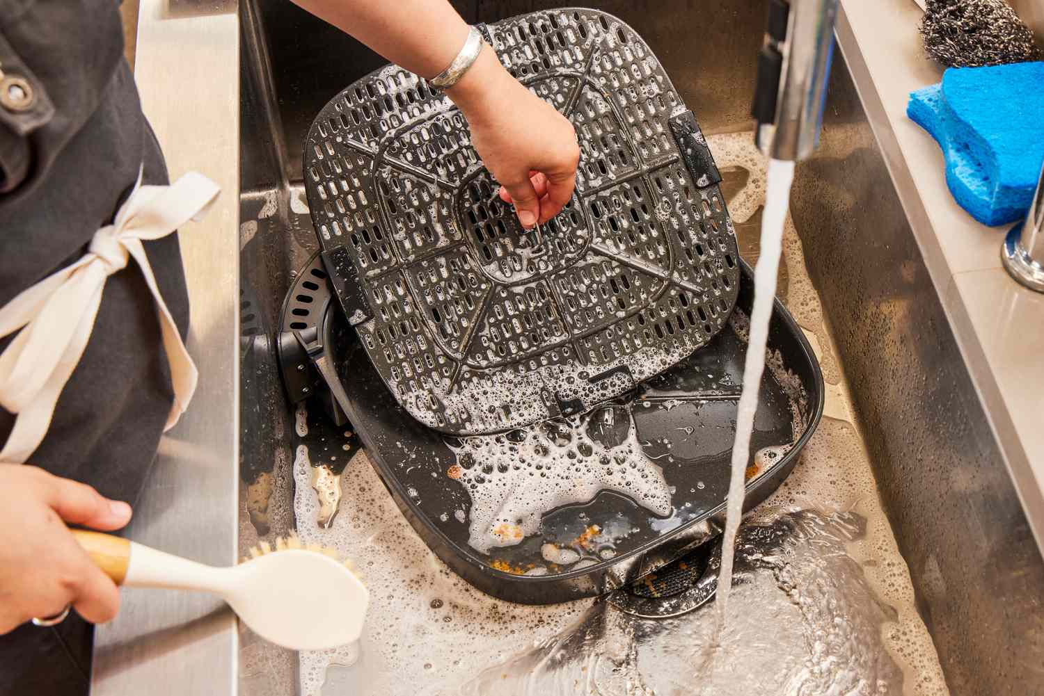 A person washing an air fryer basket in the sink.