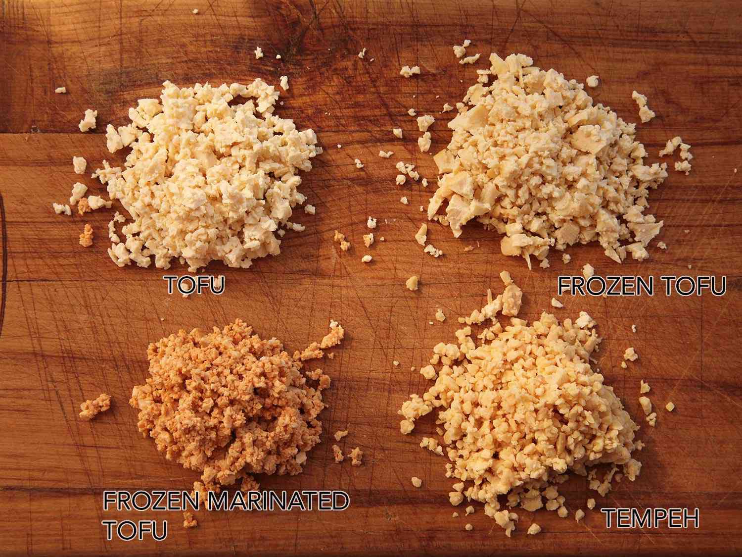 Three piles of tofu crumbles and one of tempeh. Of the tofu, one pile is plain, one has been frozen, and another has been frozen and marinated.