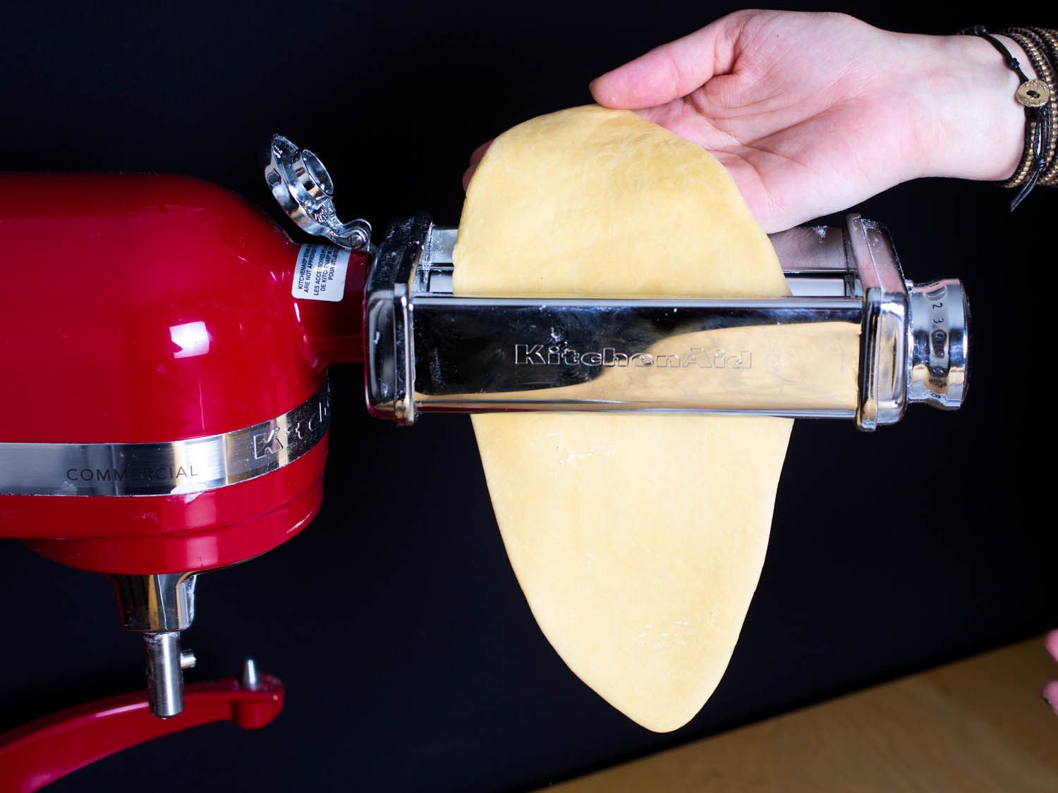 Running the slab of dough into the pasta-rolling attachment on a stand mixer. 