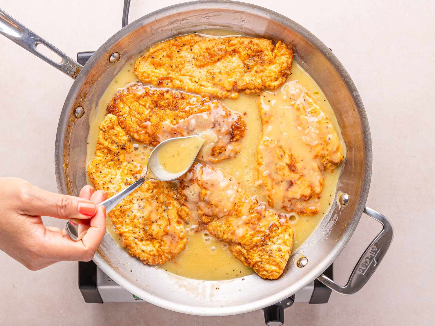 Chicken Francese being cooked in a pan hand spooning sauce over chicken