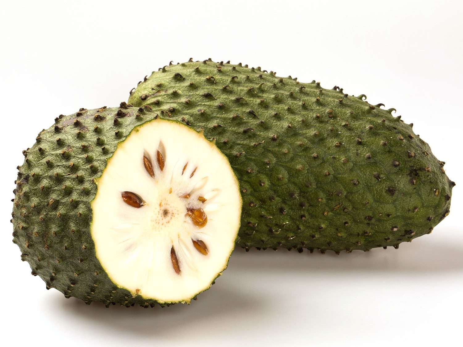A long whole soursop fruit, with a cut half of another fruit next to it showing the white interior and large dark seeds.