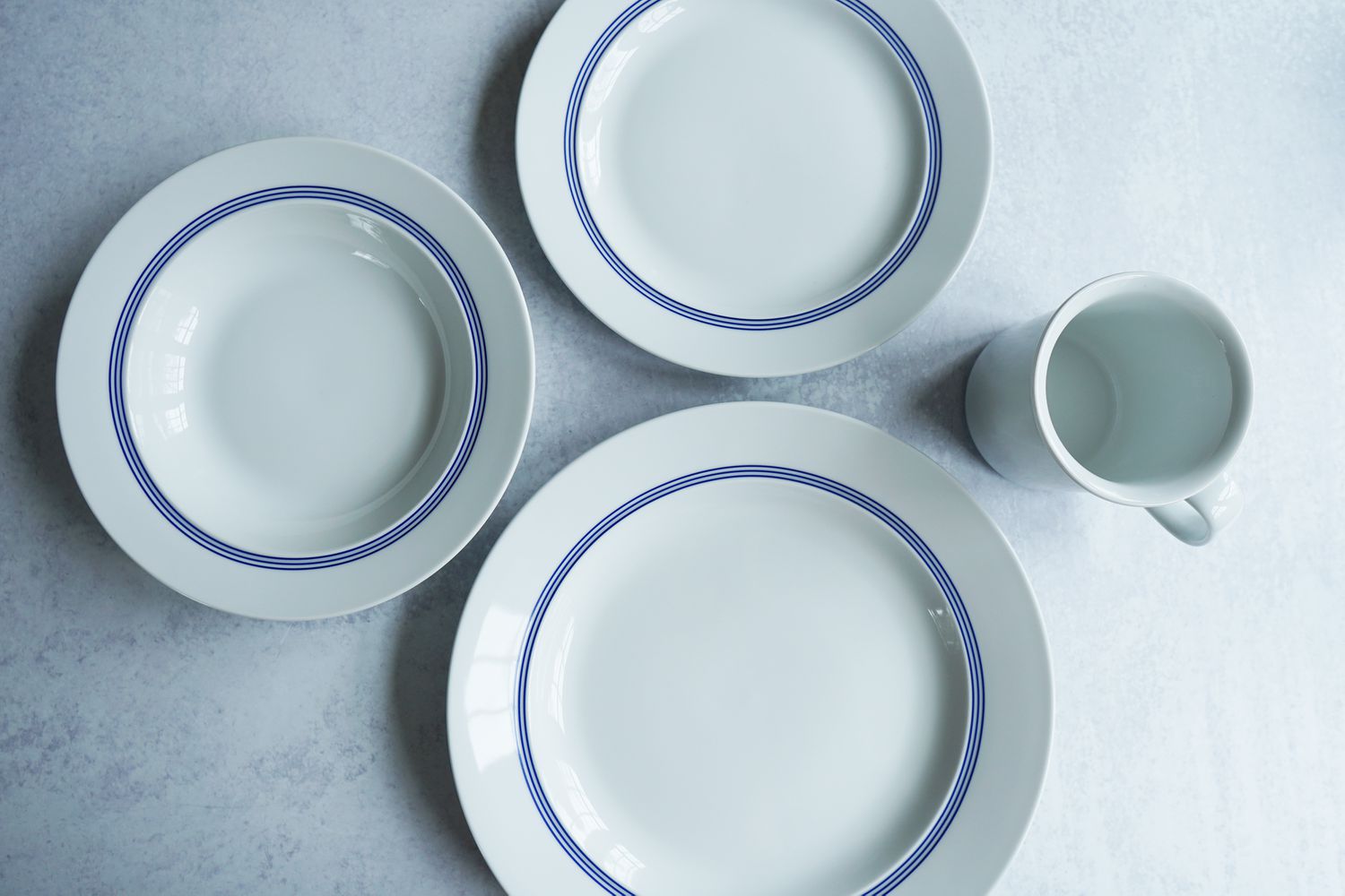 Two plates, a bowl, and a mug on a grey surface