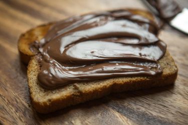 A slice of bread with a generous smear of chocolate hazelnut spread on a wooden board.