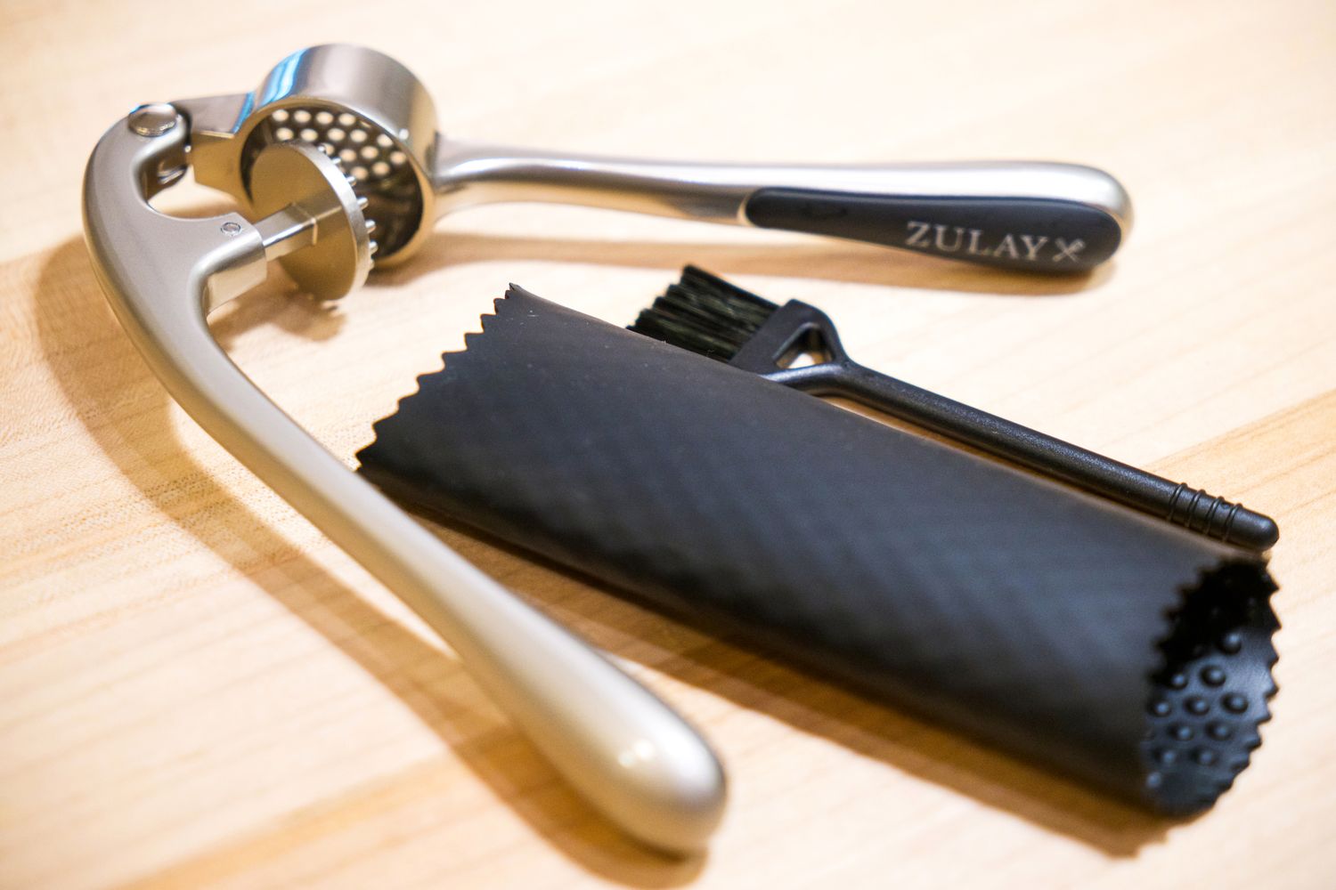 A garlic press with cleaning brush and a silicone garlic peeler laid on a countertop
