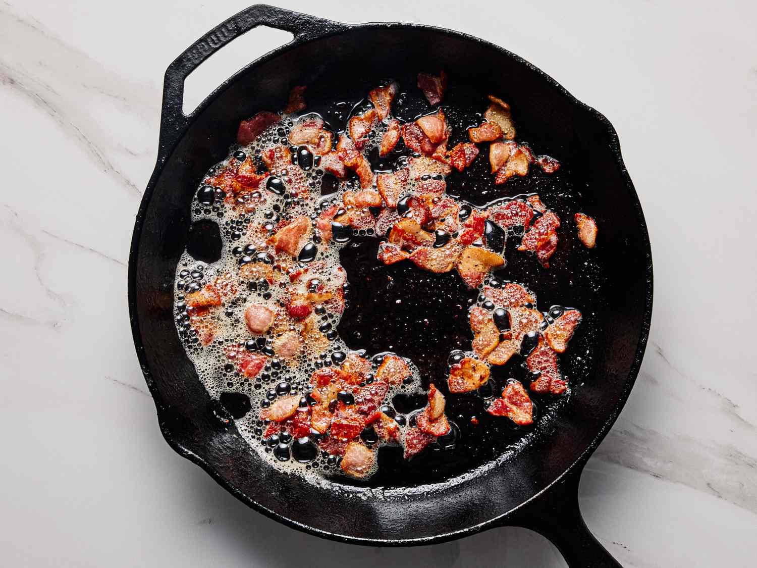 Bacon cooking in a cast iron skillet on a marble surface