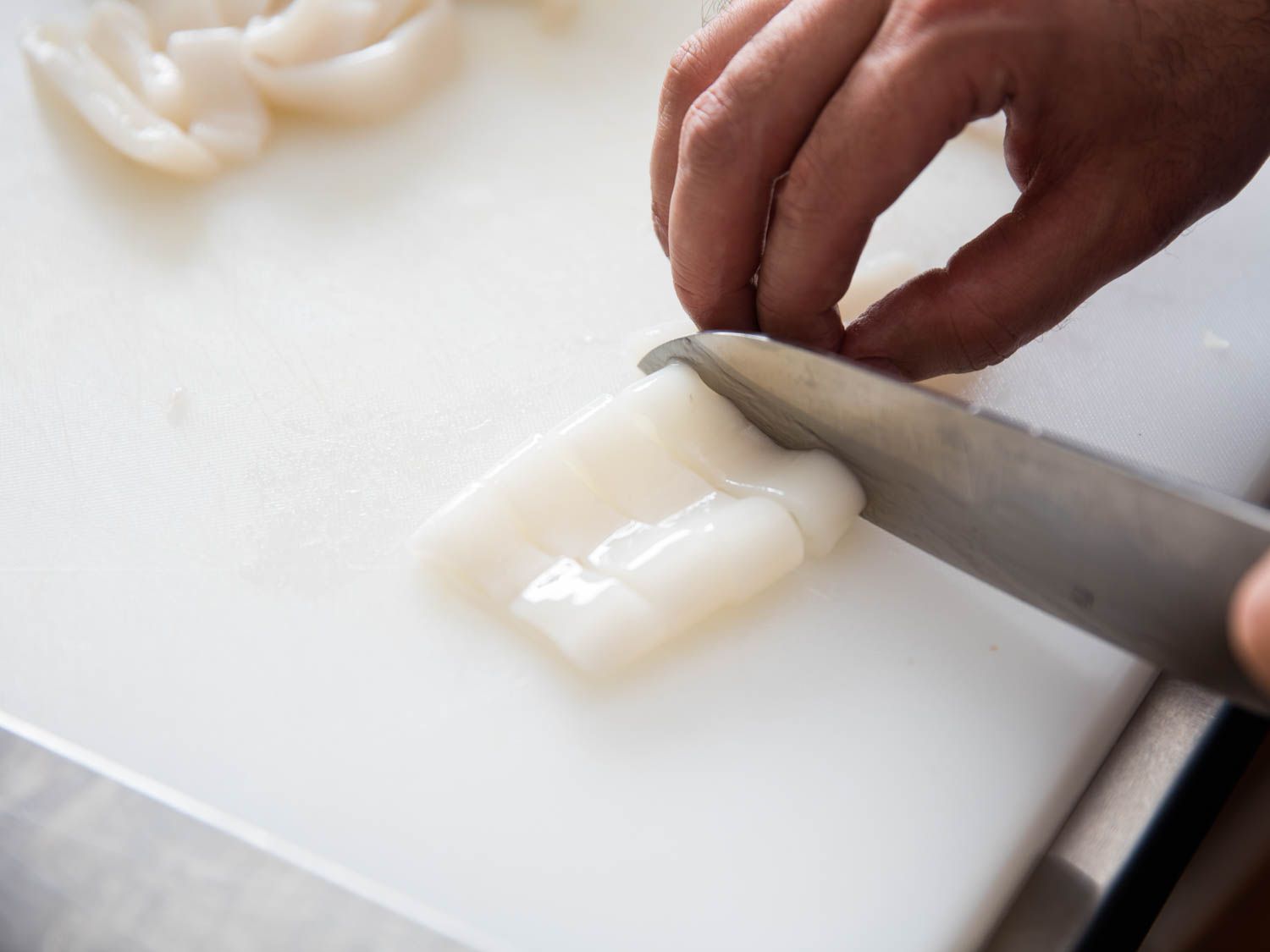 Author slices squid on a white cutting board into half-inch thick rings.