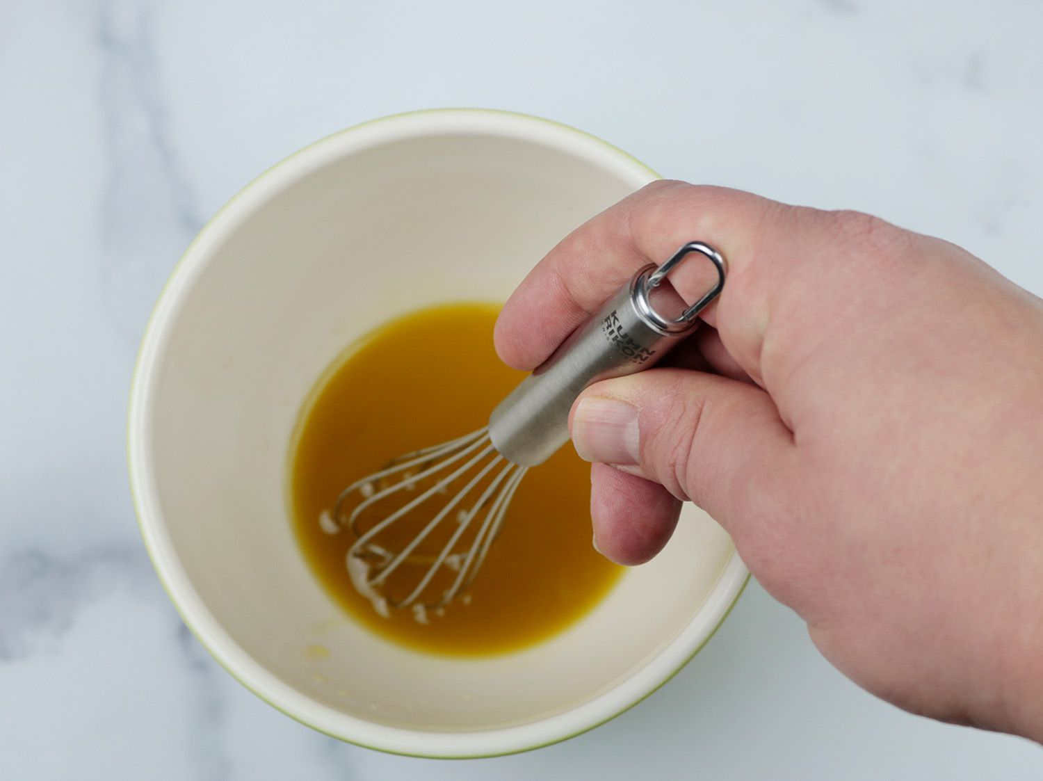 a mini whisk emulsifying a vinaigrette dressing in a ceramic bowl
