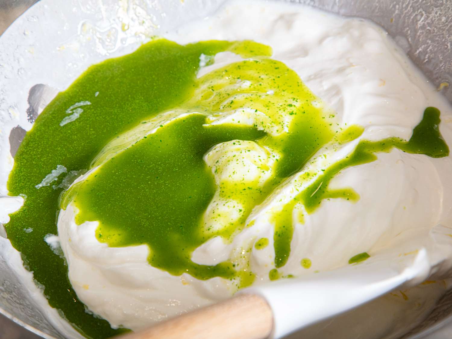 Bowl of creamy dip with green sauce being mixed with a spatula