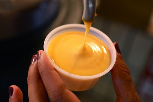 Cheese sauce being dispensed from a pump into a small plastic cup.