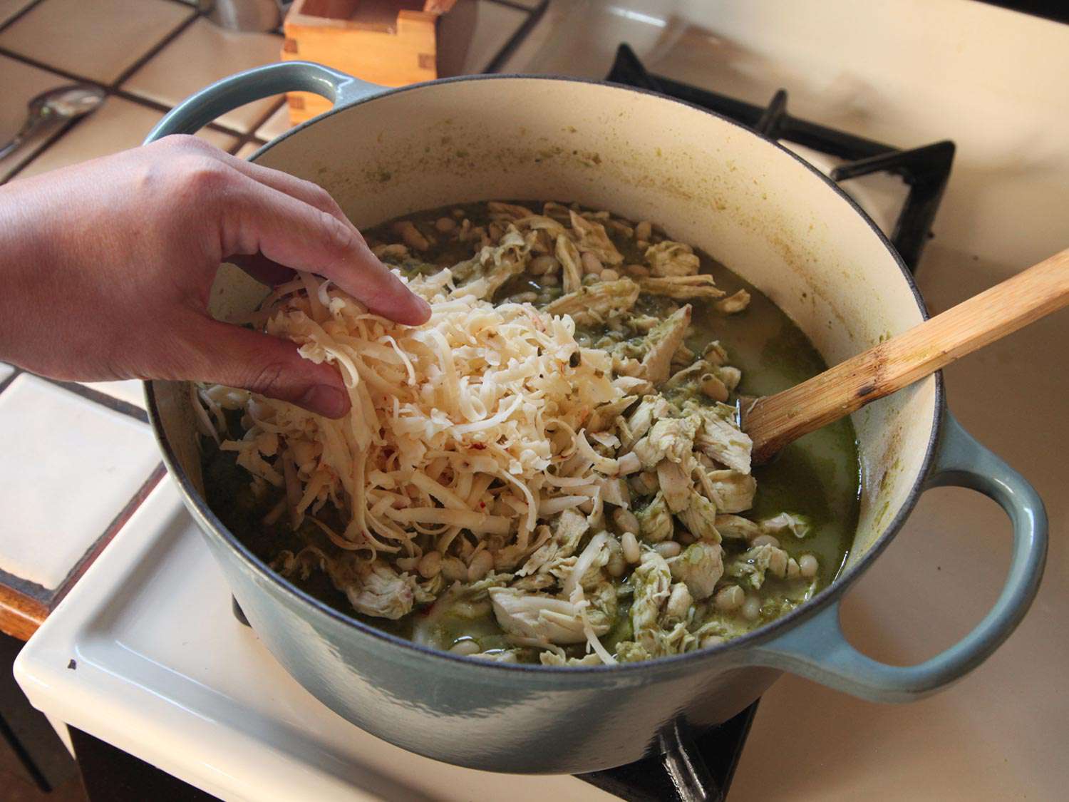 Adding shredded cheese over shredded chicken in the pot of green chili.