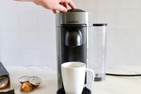 A hand pressing the top of the Nespresso VertuoPlus Coffee and Espresso Machine by De'Longhi