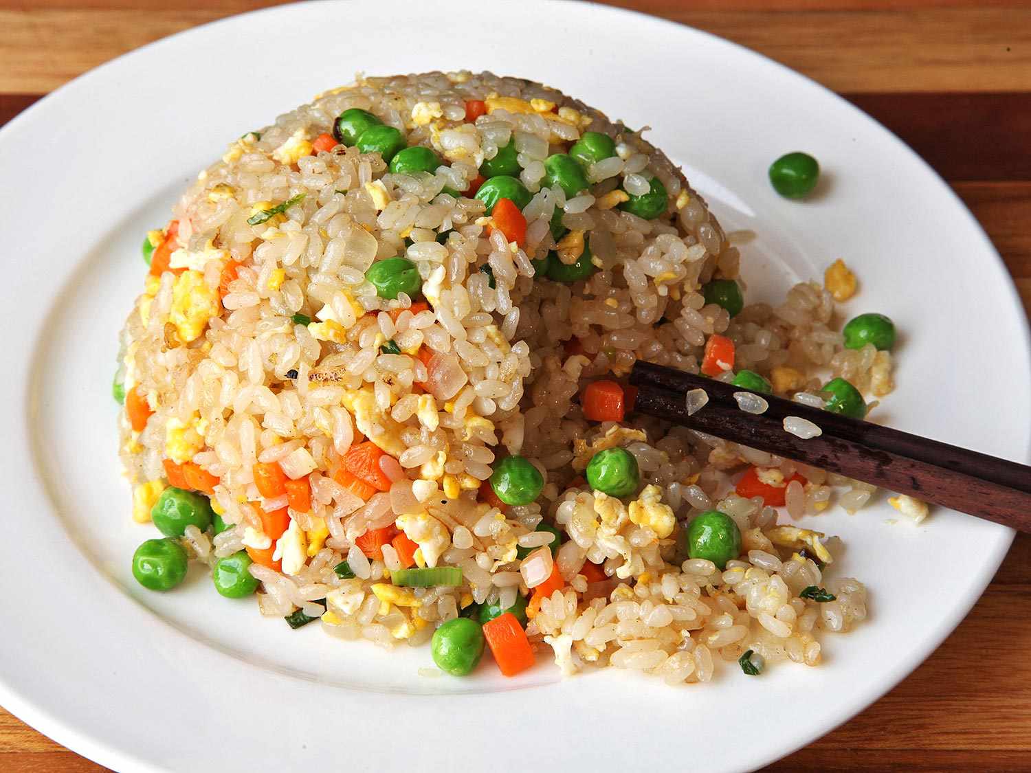 Closeup of a spherical mound of easy vegetable fried rice. Chopsticks have caused an avalanche on one slope of the mound.