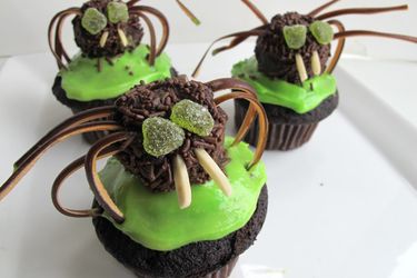 Three chile-chocolate spider cupcakes, presented on a square white plate.