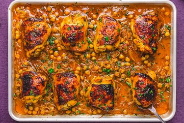 Baked chicken thighs with chickpeas on a tray garnished with herbs in a savory sauce