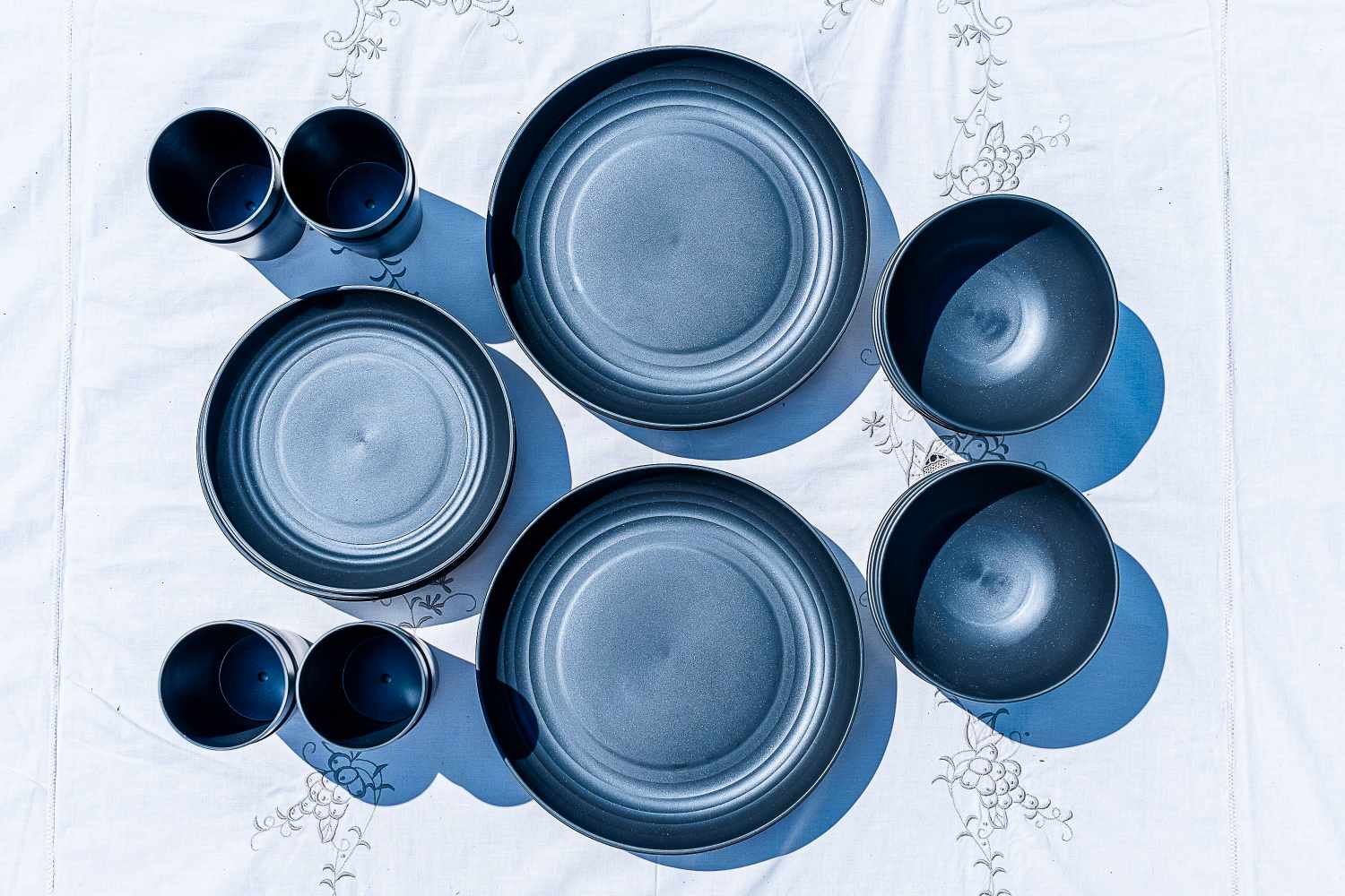 A collection of Tevio Plastic Wheat Straw Dinnerware Set tableware including plates bowls and cups arranged on a patterned tablecloth