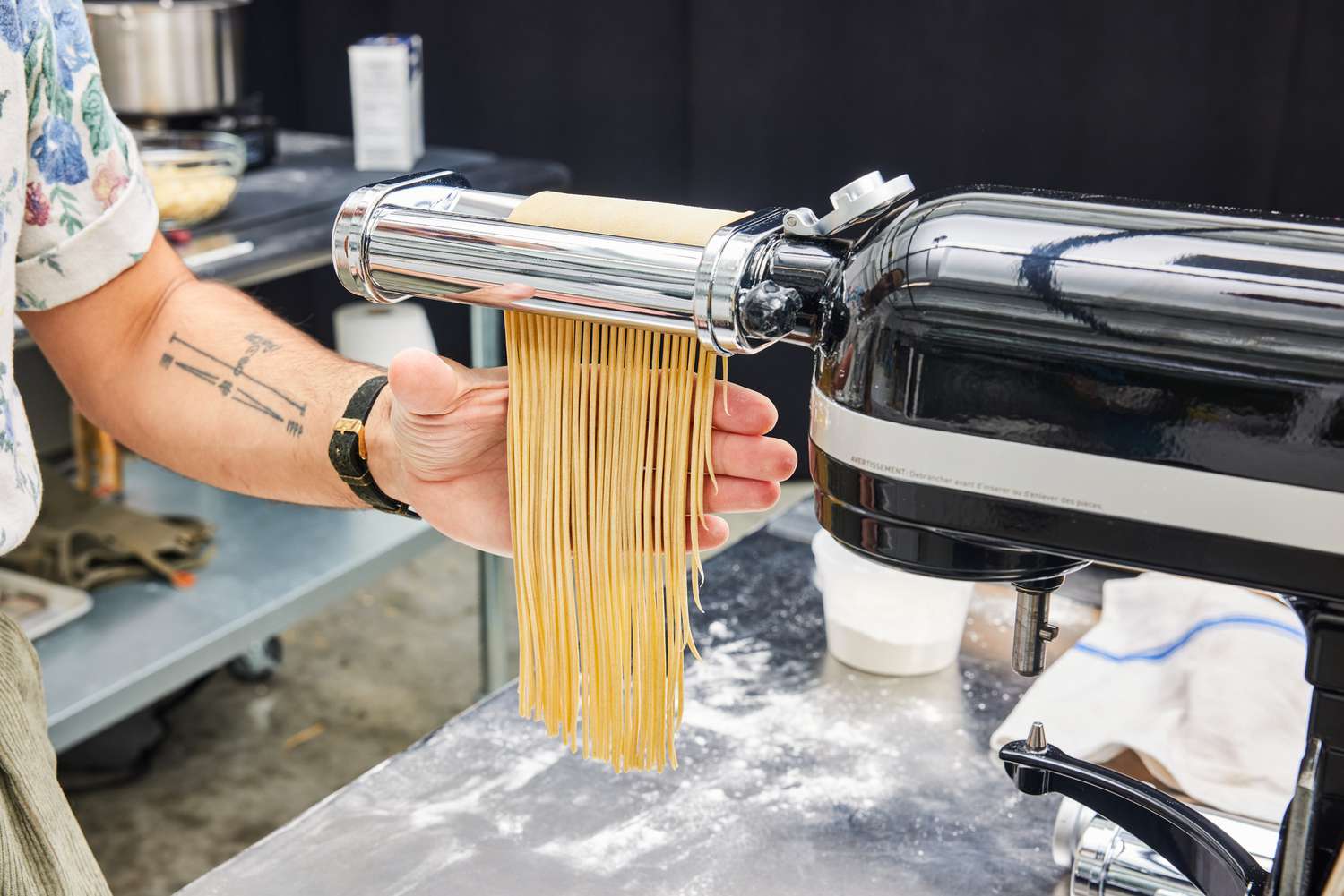 A person using a KitchenAid attachment to cut pasta into spaghetti