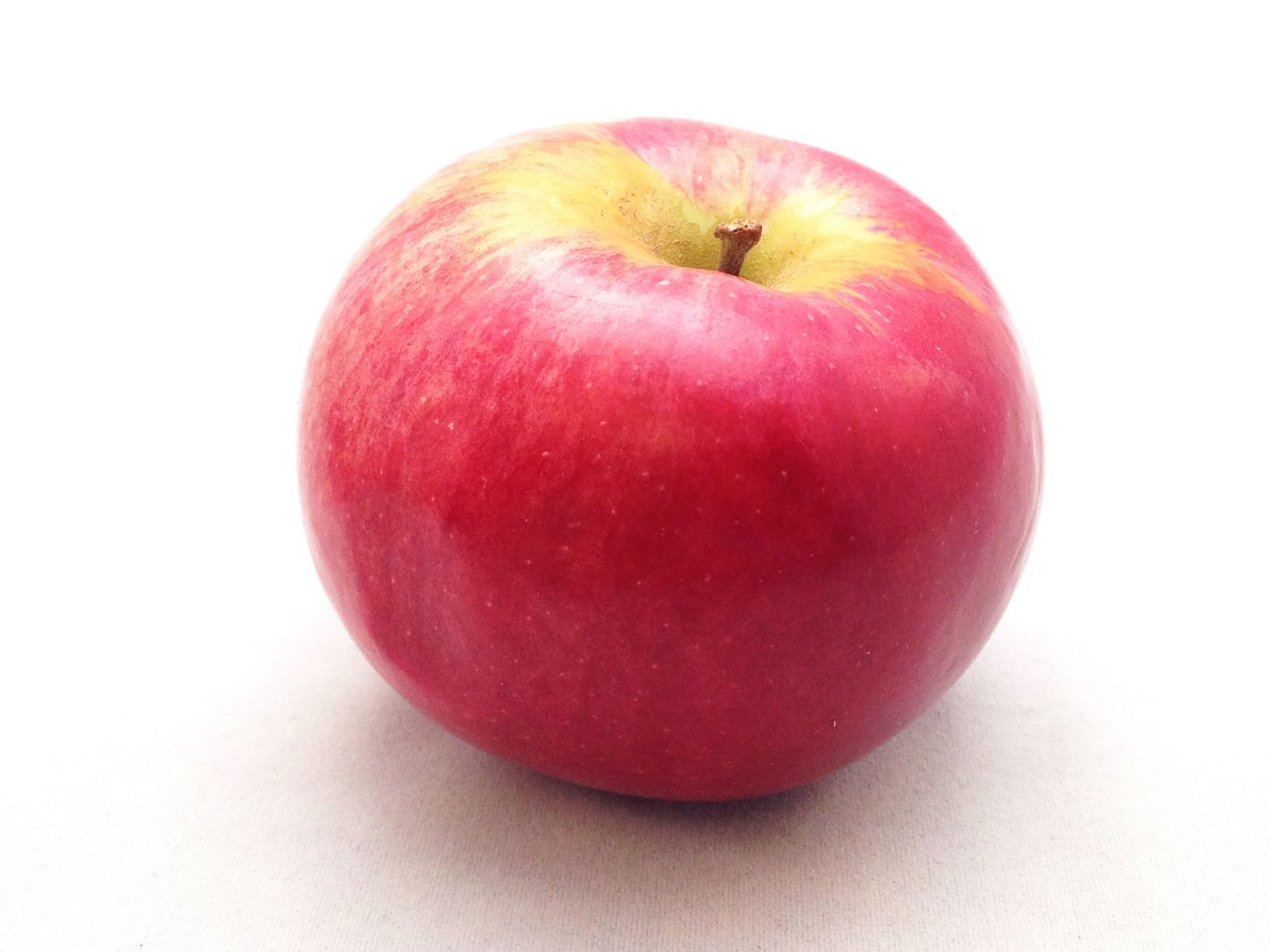A single apple placed on a white surface