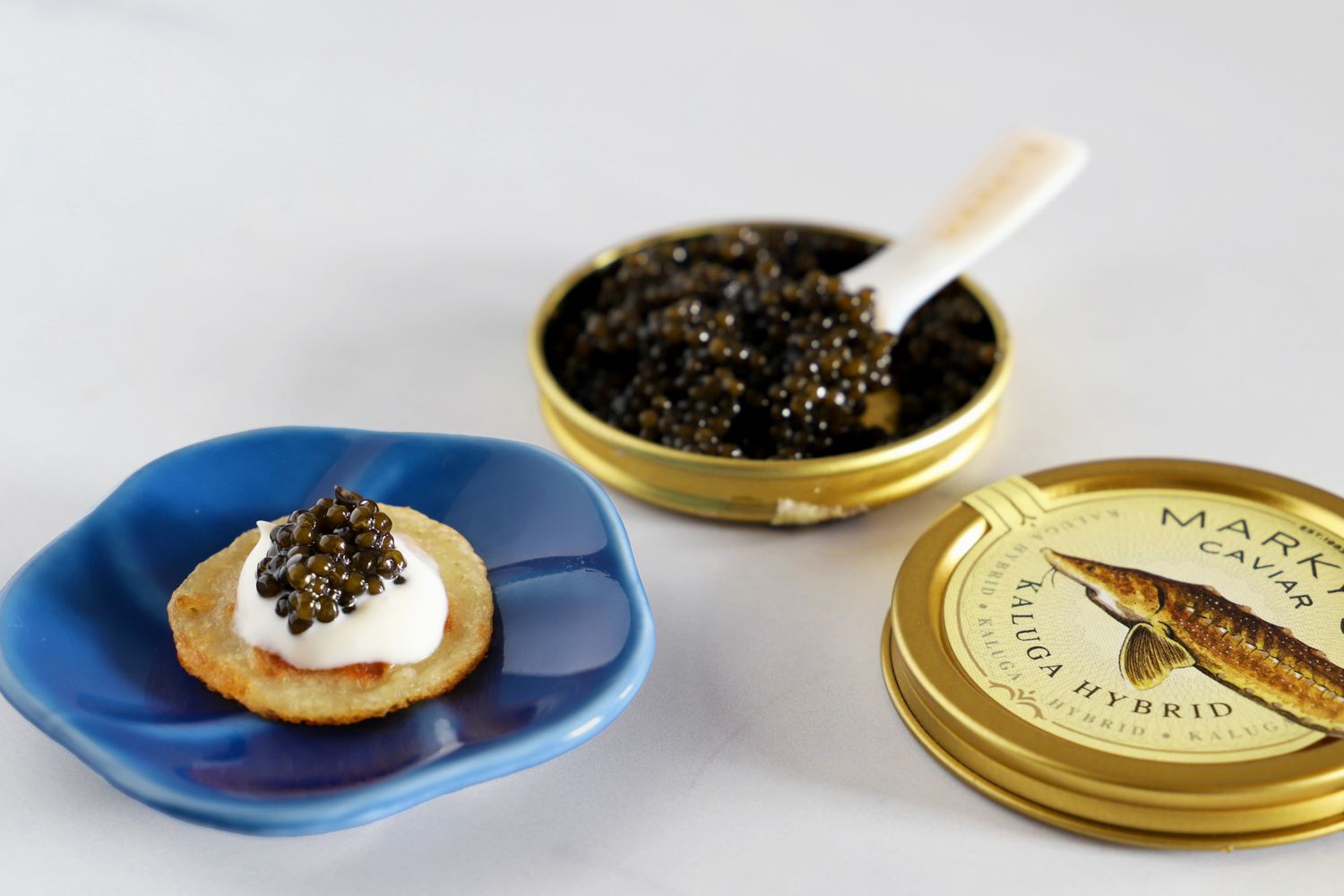 A tin of kaluga hybrid caviar next to a prepared blini topped with crème fraîche and caviar