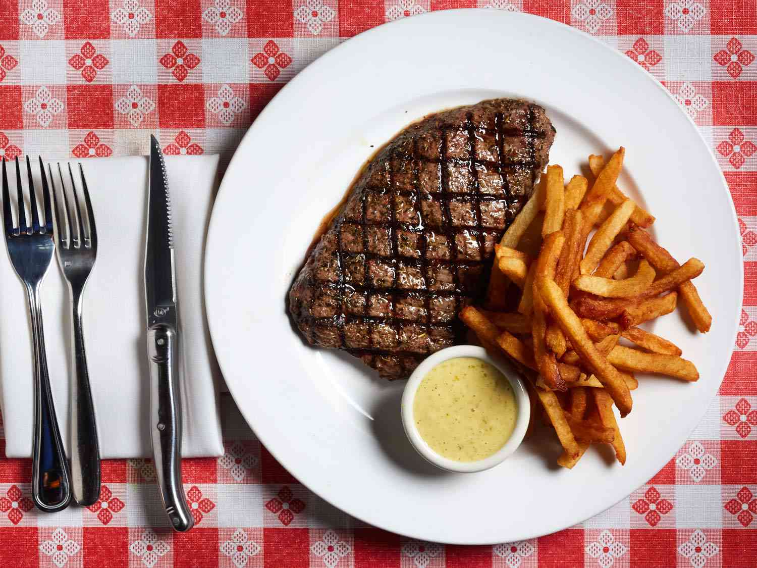 A ribeye and French fries at Bistrot du Coin on a classic red-checked tablecloth.