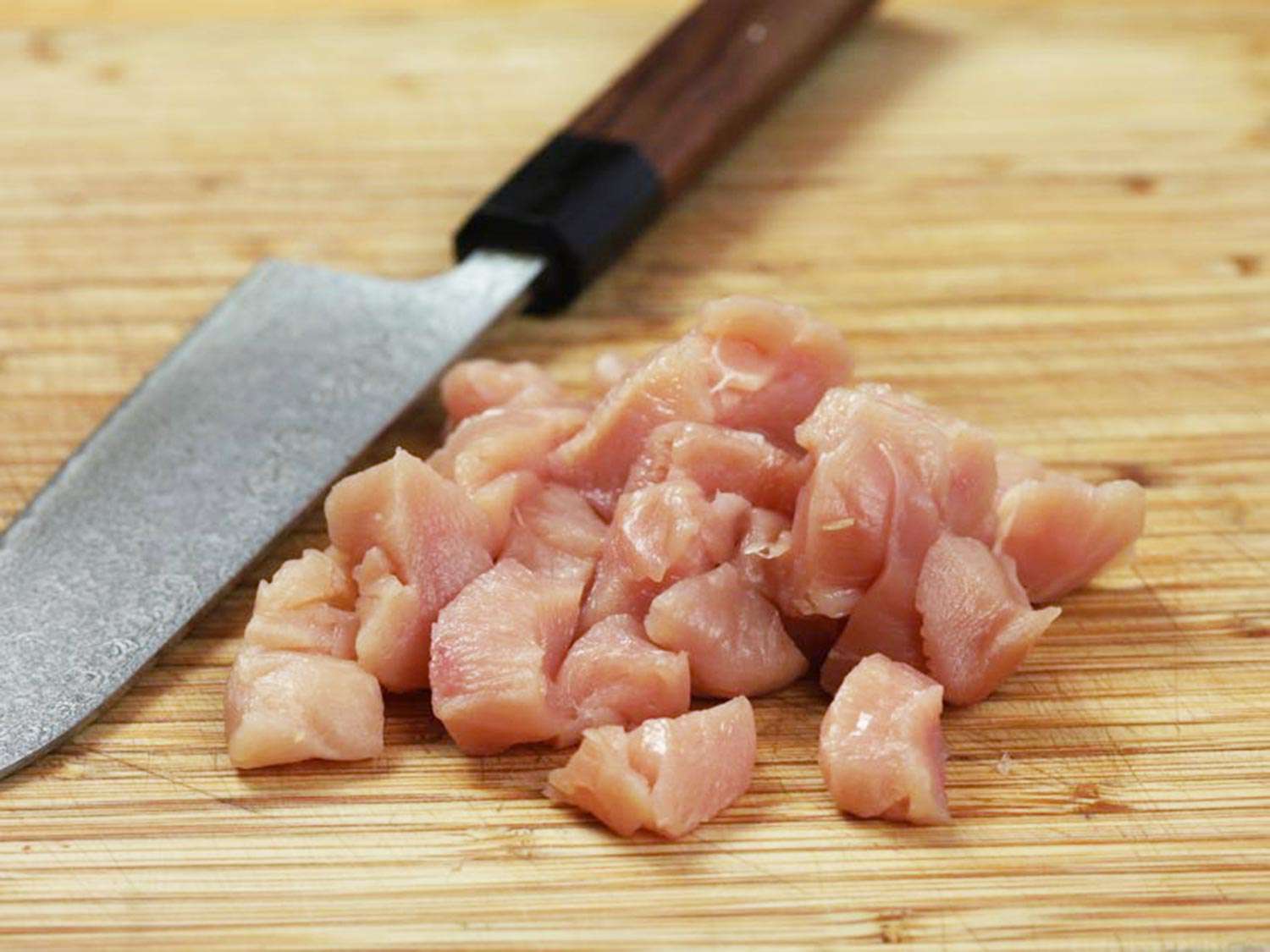 Chicken breast cut into bite-size cubes on a bamboo cutting board next to a knife.