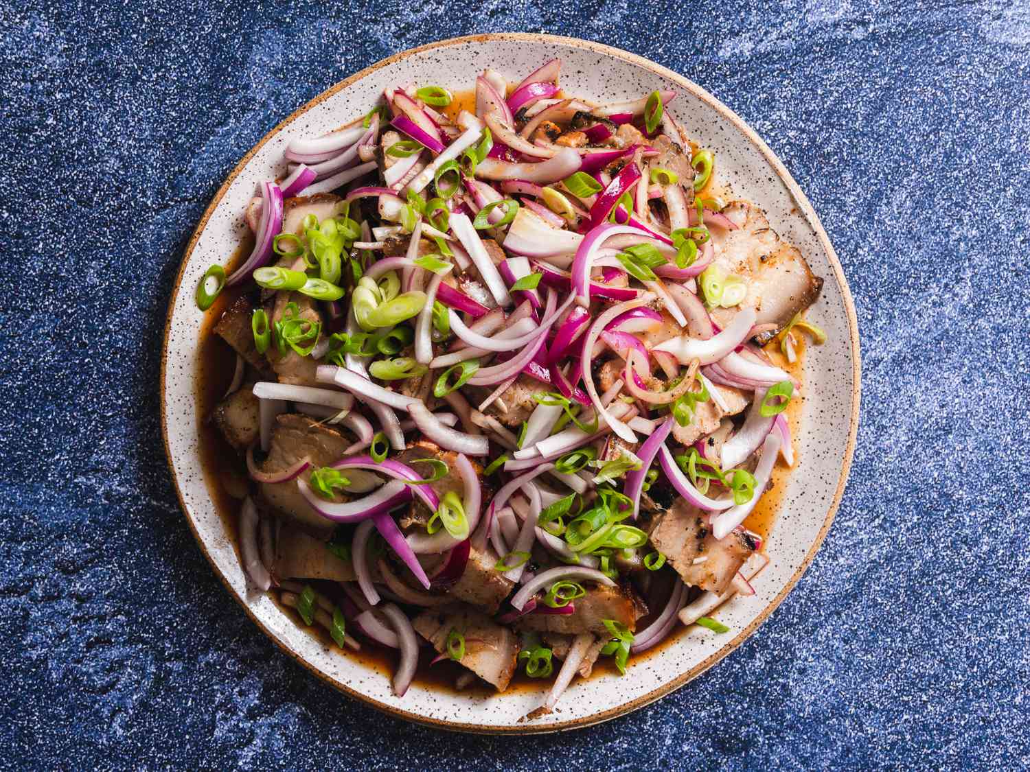 A platter Kilawin: marinated and grilled pork belly tossed in vinegar-based dressing and topped with sliced red onion and scallions
