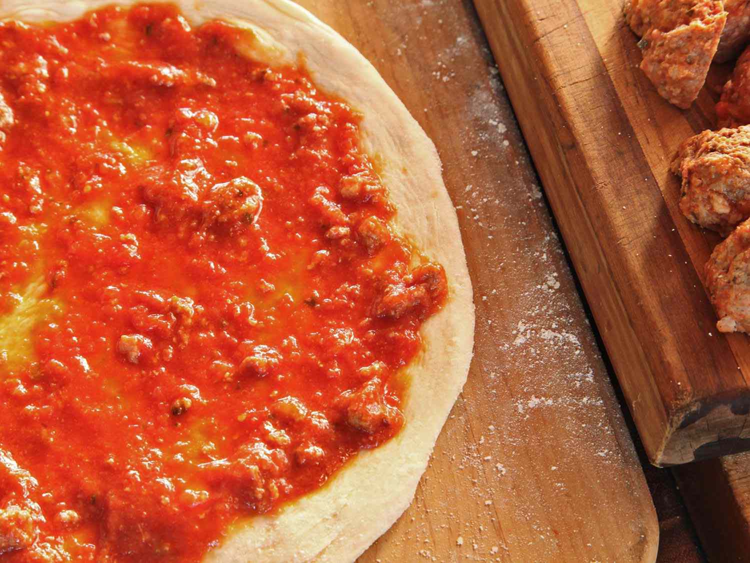 Meatball-laced tomato sauce spread over an unbaked pizza crust