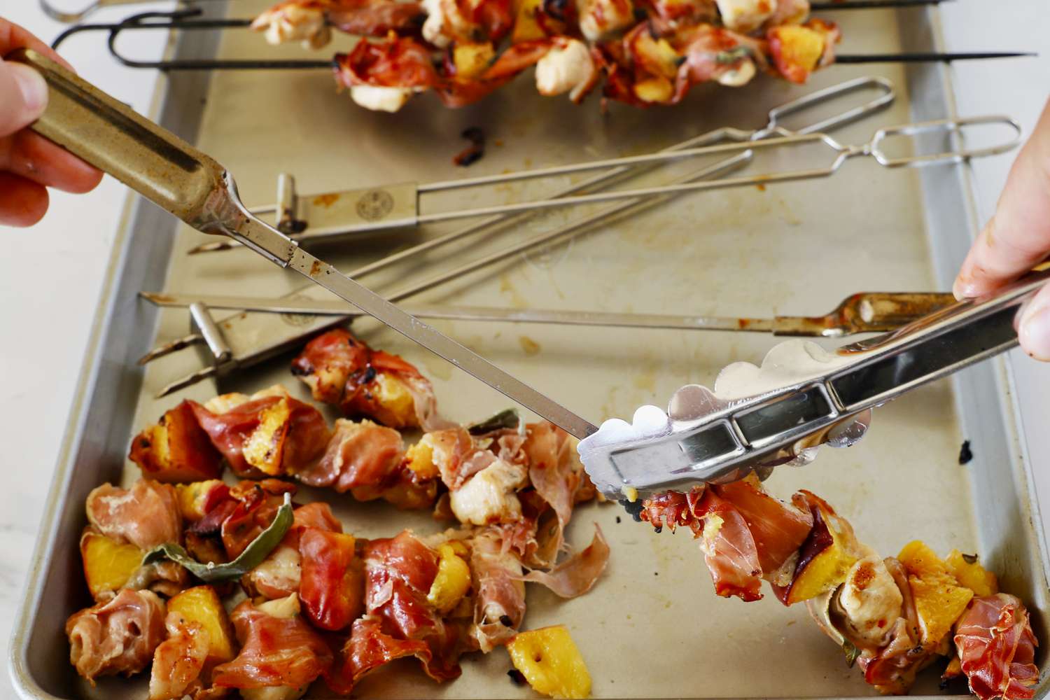 A person pulling grilled meat off of skewers.