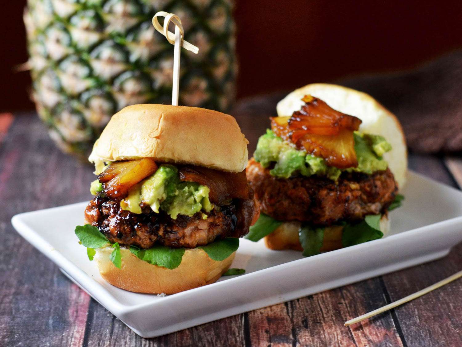 Mini pineapple-teriyaki-glazed salmon burgers, served on a small rectangular plate.
