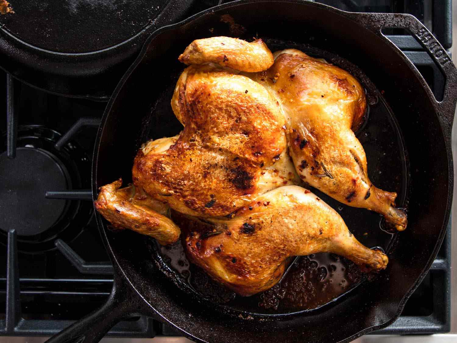 A spatchcocked chicken cooked under a brick in a cast iron skillet with golden-brown skin.