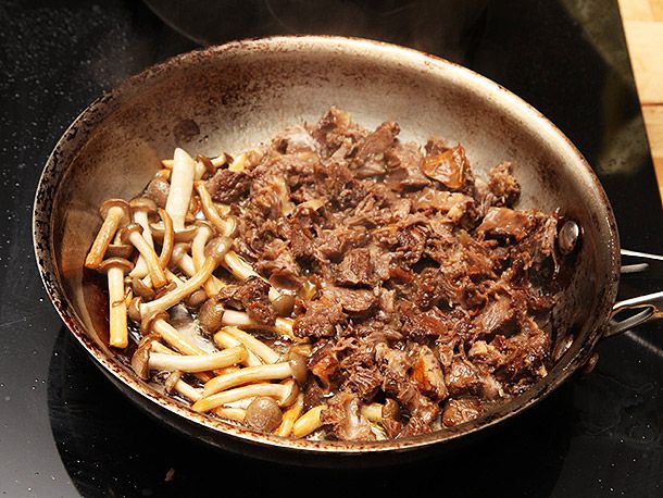Shredded short rib meat being sautéed in a skillet with hon shimeji mushrooms.