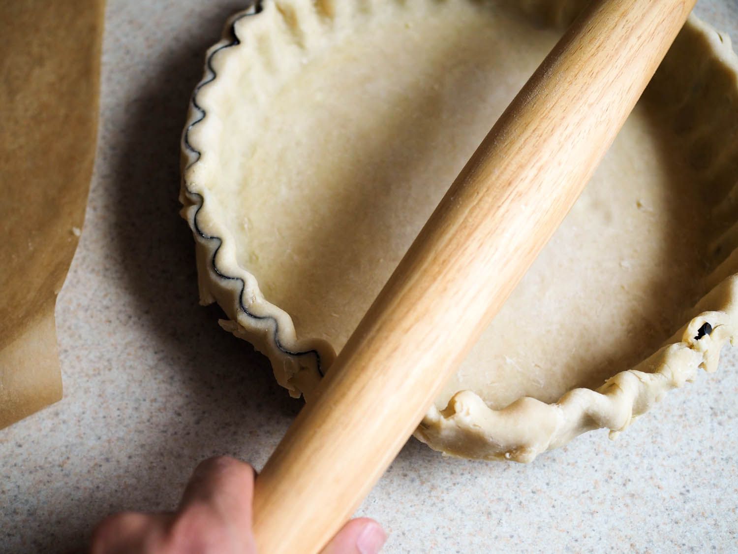 Fluted tart pan is lined with rolled out pie dough. A rolling pin is rolled over the top to trim away the excess.