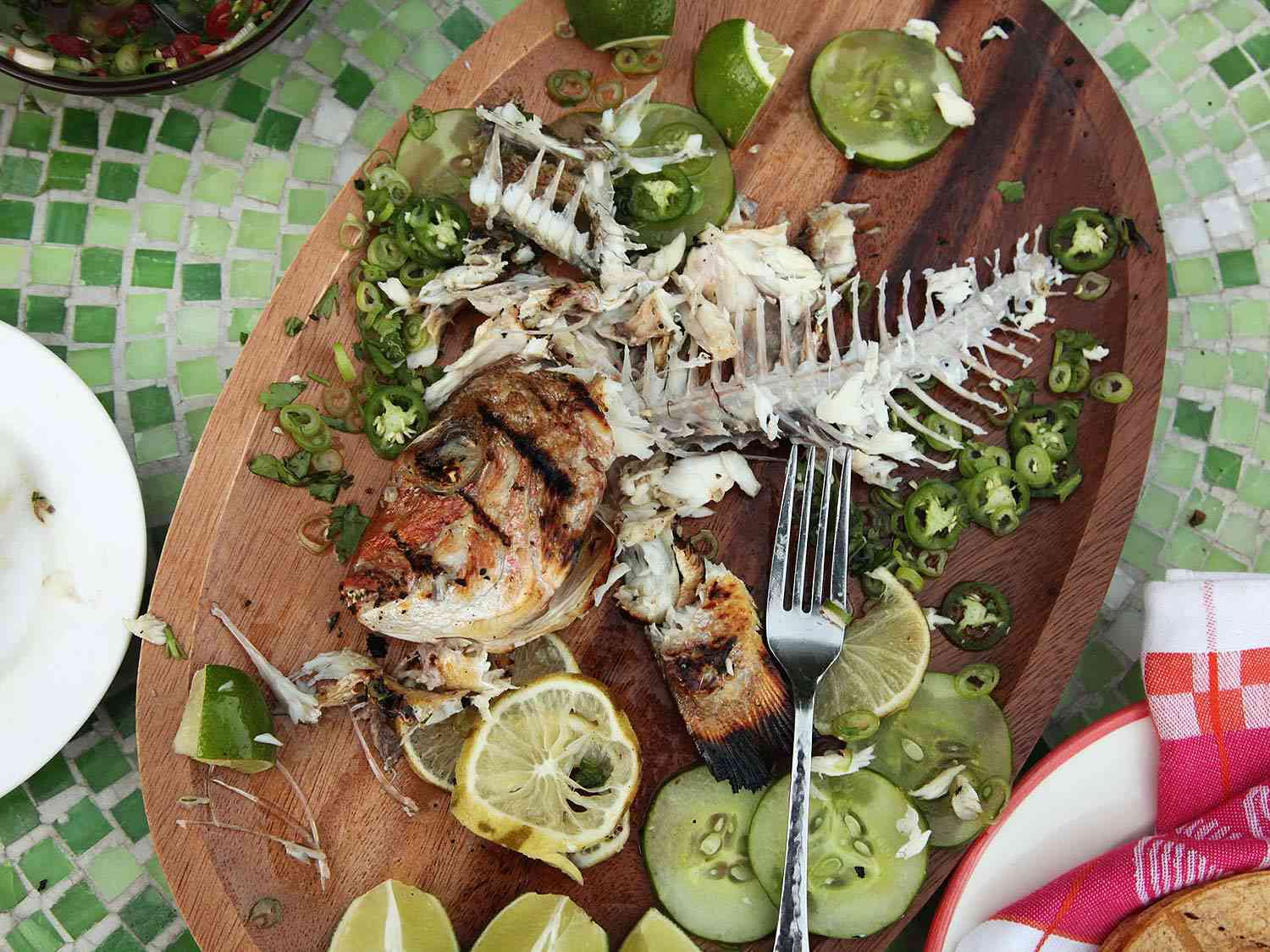 A grilled fish that has been eaten, only bones remain on a serving platter. 