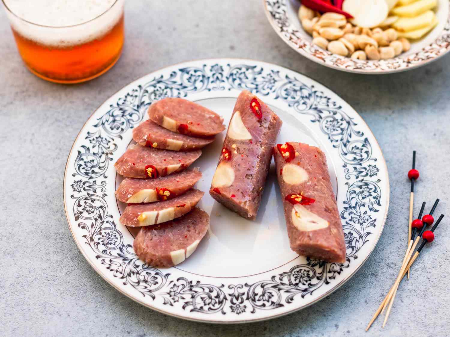 A plate of sliced nem chua, flanked by toothpicks for serving and a glass of beer.