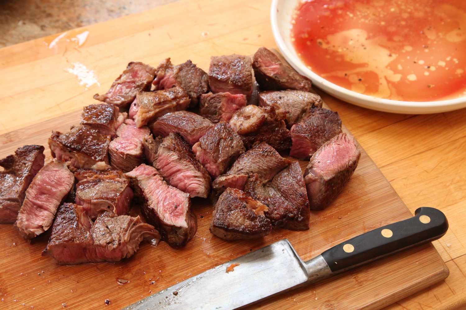 Cubes of seared beef on wooden cutting board next to chefs knife