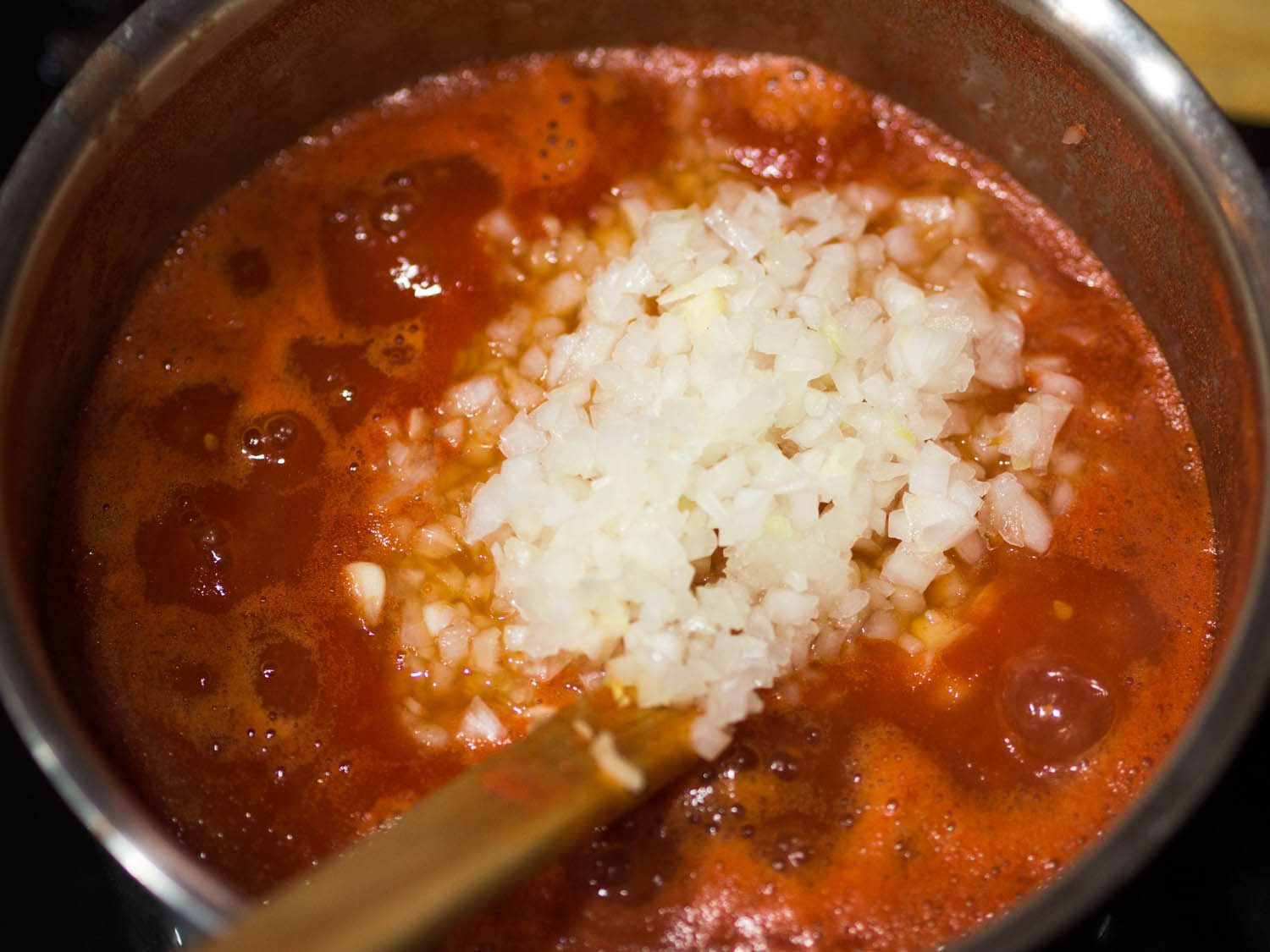Raw diced onion being added to fresh tomato sauce