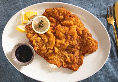 Plate of wienerschnitzel with lemon slices and dark sauce on the side