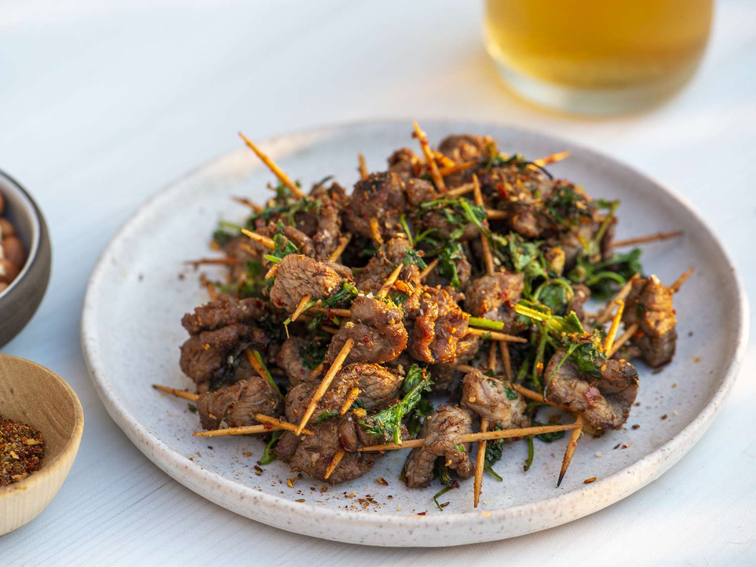 Plate of toothpick lamb set in front of out of focus glass of beer in background