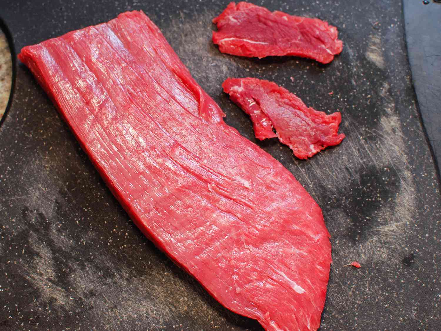Pieces sliced off a raw whole slab of flank steak 