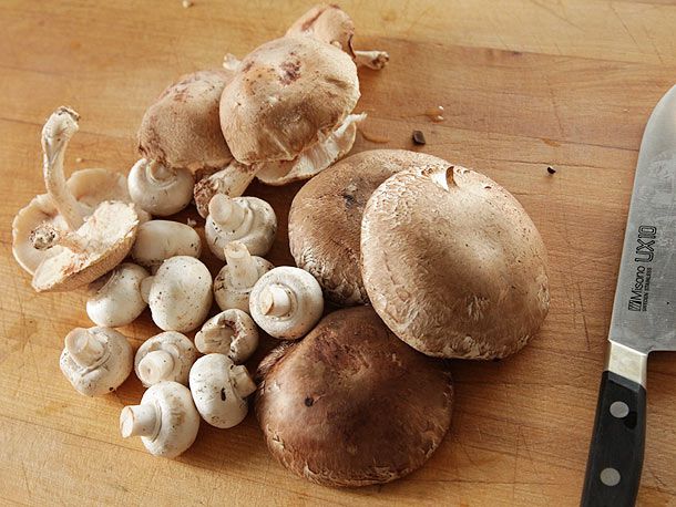 Shiitake, button, and portobello mushrooms on a cutting board next to a chef's knife.