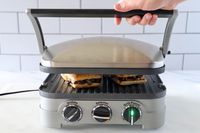 A person lifting the lid of the Cuisinart panini press as it's cooking two sandwiches.