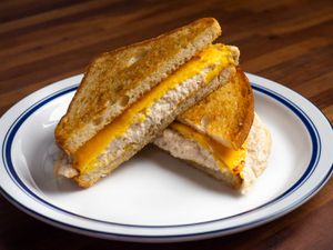 A tuna melt sandwich on a plate, cut in half diagonally to make triangles; showing melted yellow American cheese slices on top of a creamy tuna salad and nicely toasted bread.