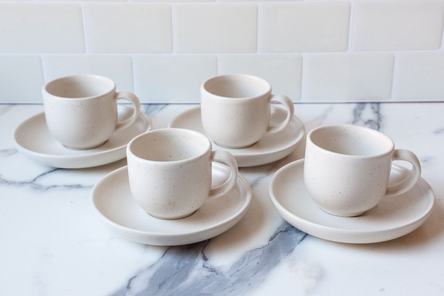 Four espresso cups on saucers on a marble countertop.